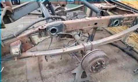 A classic muscle car in primer grey sits partially restored in an auto body workshop.