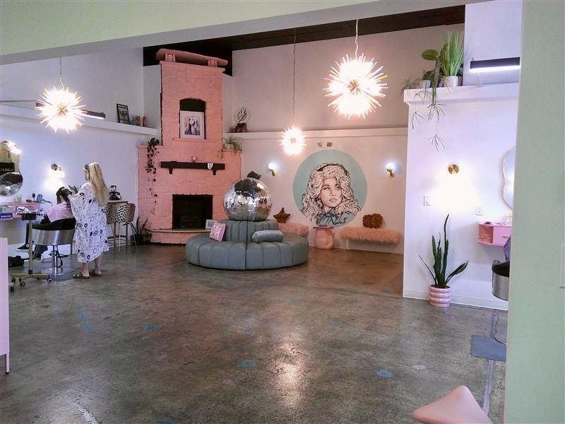 Spacious pink salon with a central styling chair, mirrors, plants, and modern starburst lights