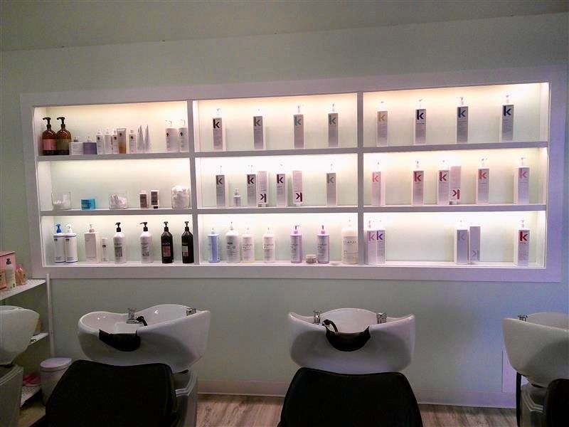 Modern salon interior with lit product shelves and black shampoo chairs