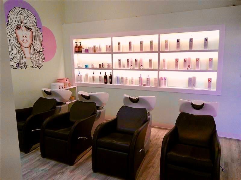 Modern salon with black shampoo chairs, white sinks, and backlit shelves of hair products