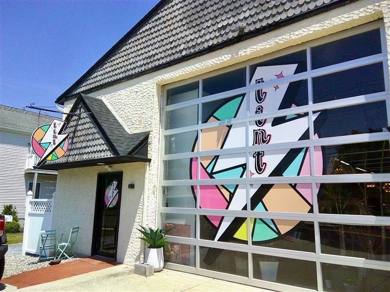 Colorful storefront with a large geometric window mural and a dark shingled roof under a clear blue sky
