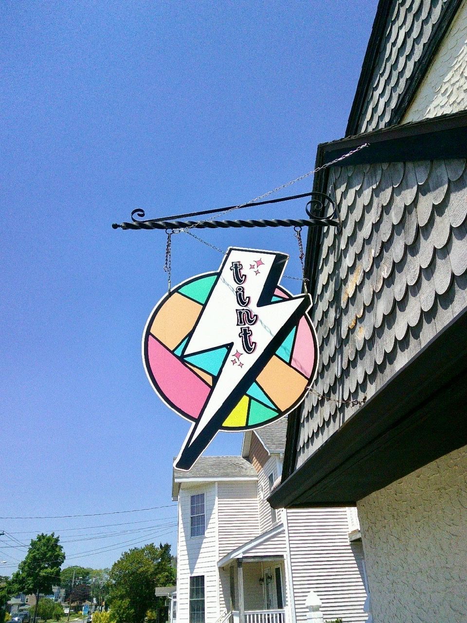 Colorful round sign with a white lightning bolt hanging over a house against a blue sky