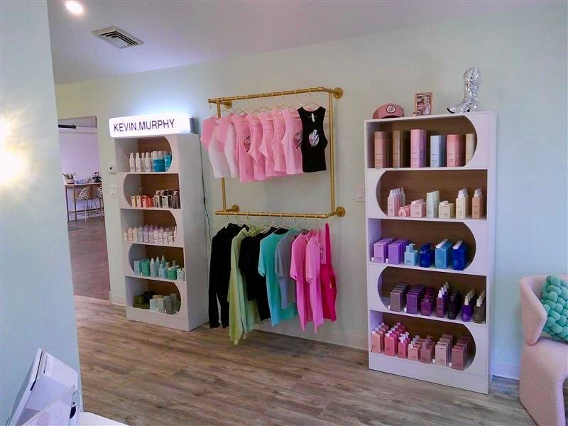 Boutique clothing display with folded shirts, hanging pastel tops, and shoes on white shelves