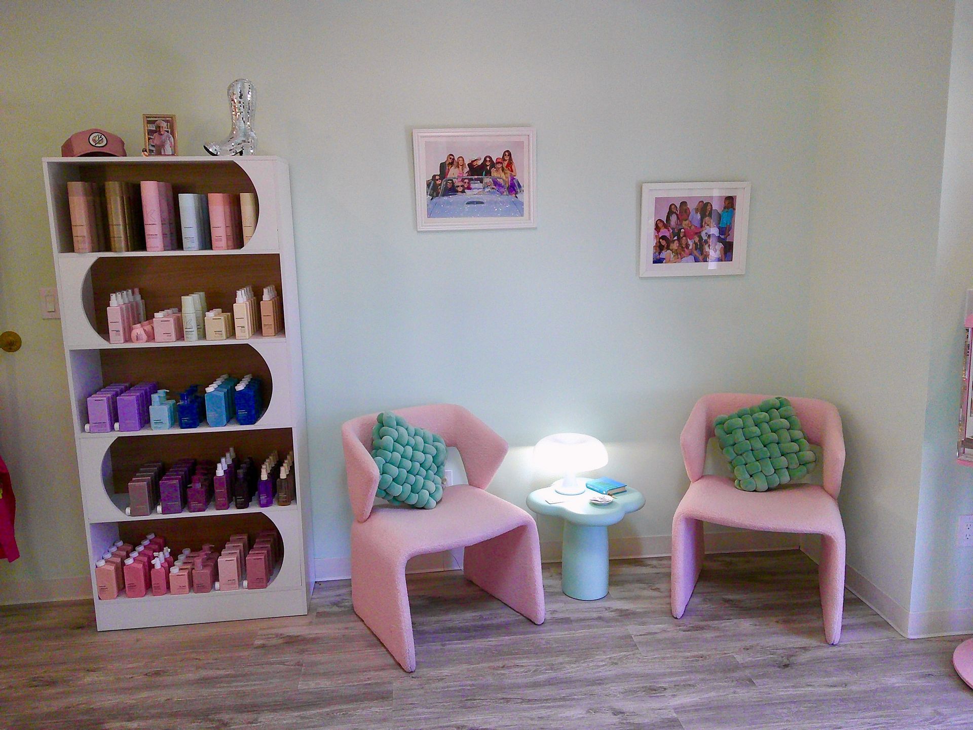 Cozy room with pink chairs, green pillows, a small table, and a bookshelf of colorful books and decor.