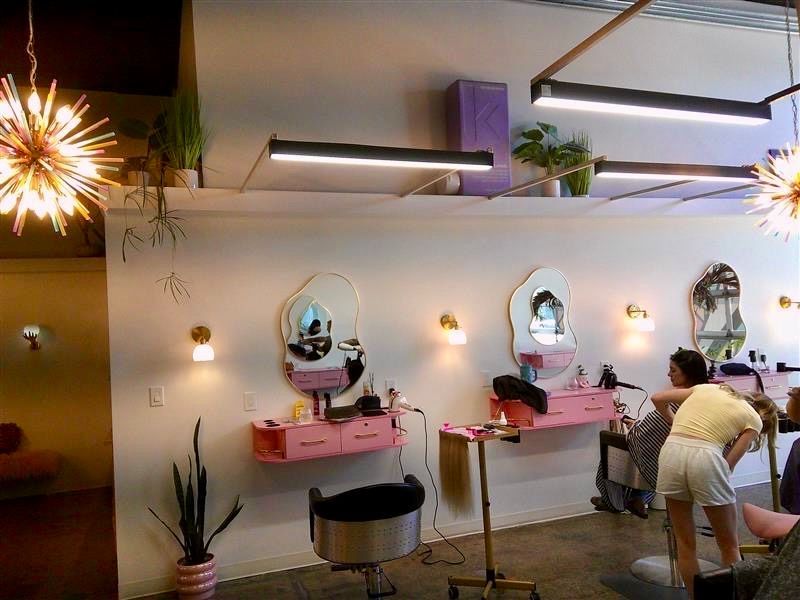Pink nail salon with mirrors, chairs, and two people at manicure stations