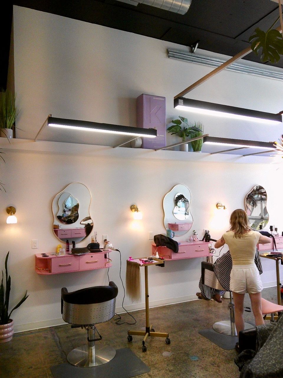 Modern salon with pink styling stations, mirrors, and a person working at a chair