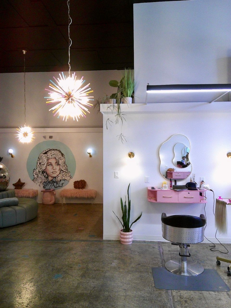 Modern salon interior with pink styling stations, pendant lights, and a wall mural in the background