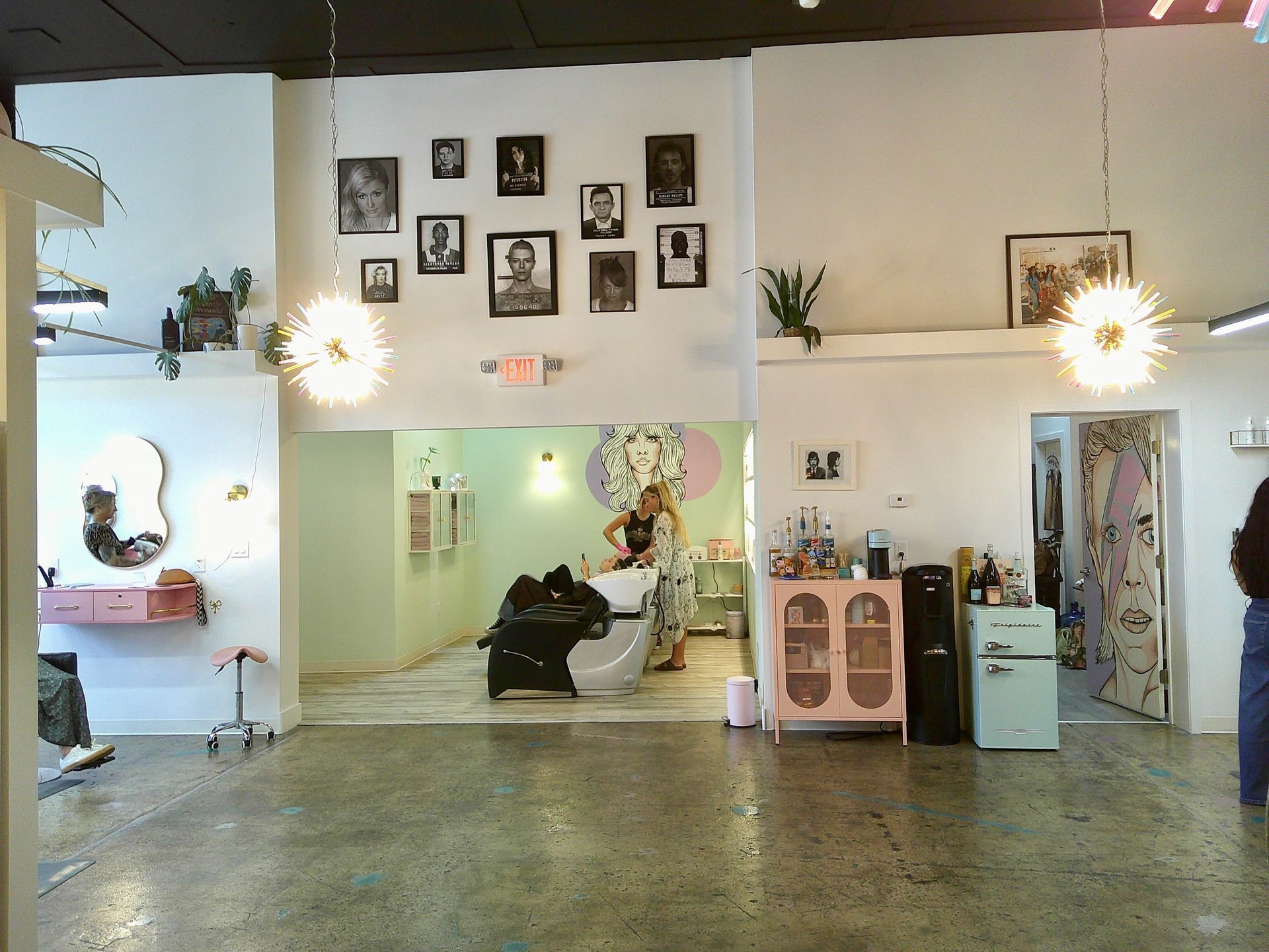 Spacious art gallery with framed portraits, hanging lights, and sculptures in a bright white room
