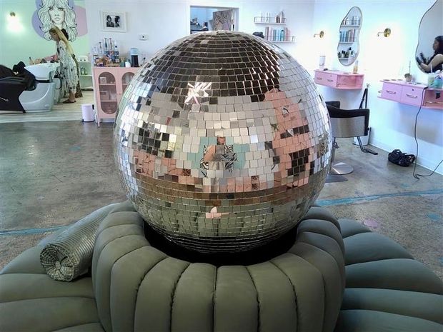 Large mirrored disco ball on a cushioned base in a pastel gallery-like room