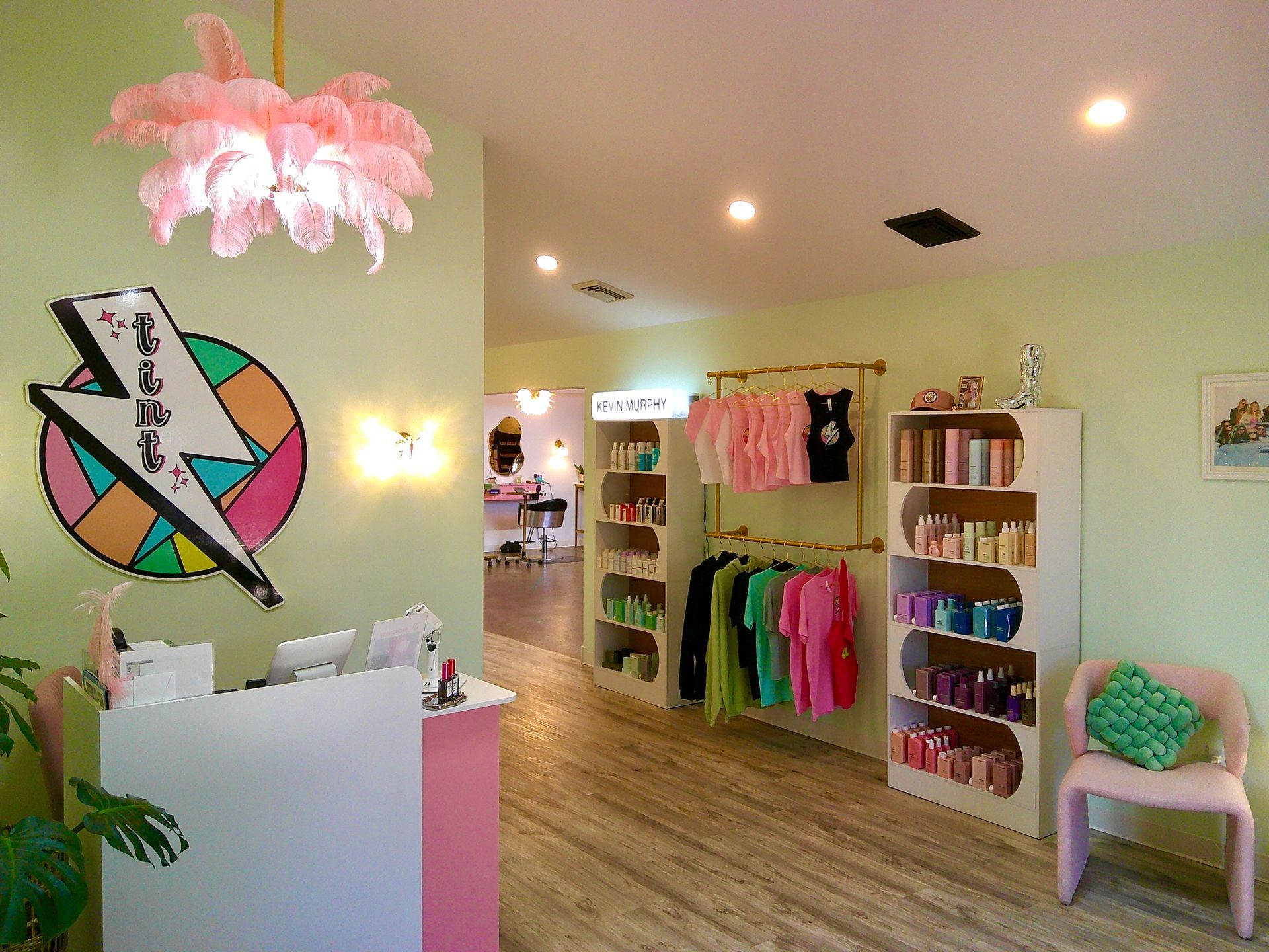 Bright boutique interior with pastel walls, clothing racks, shelves, a counter, and a pink chandelier