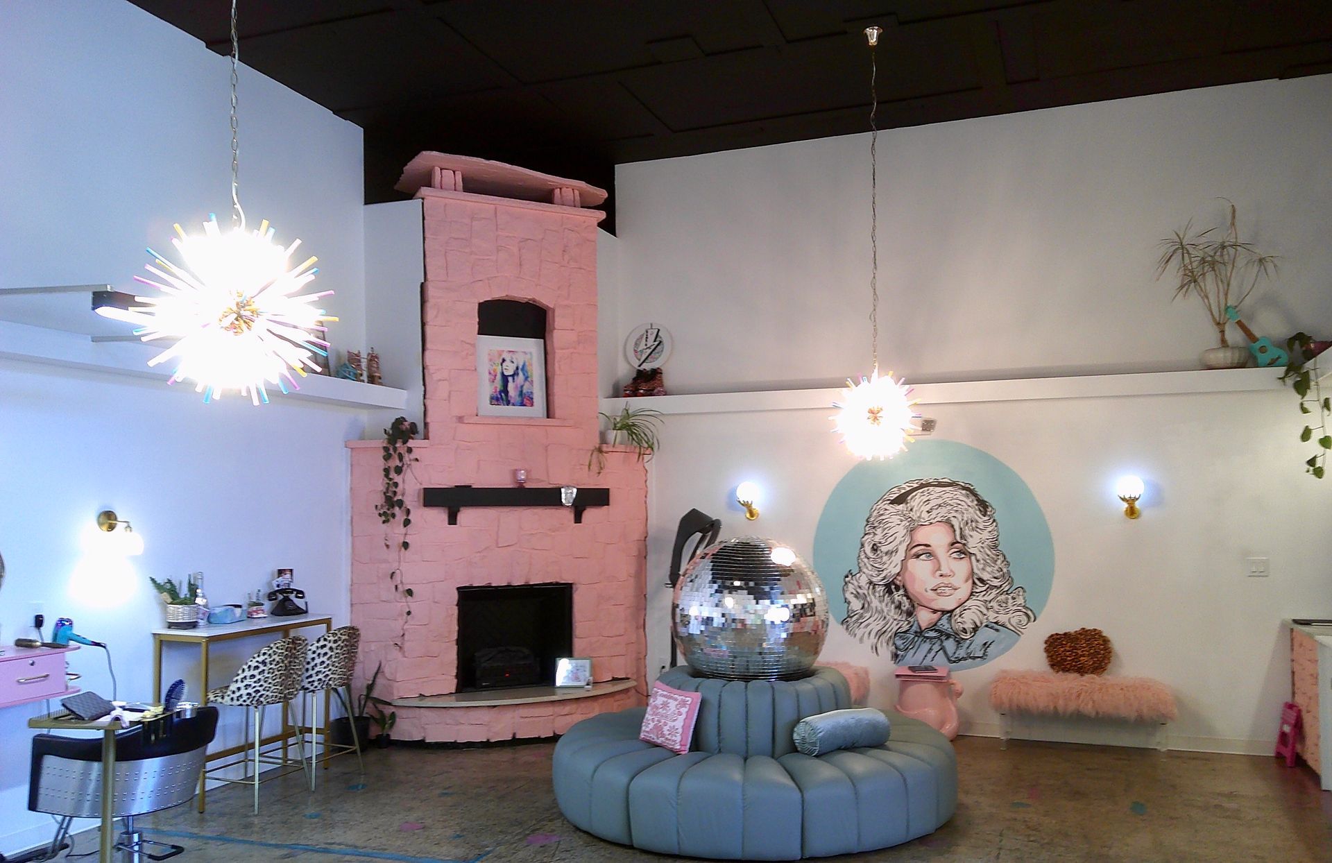 Pink fireplace lounge with blue circular sofa, hanging lights, and large portrait mural on the wall