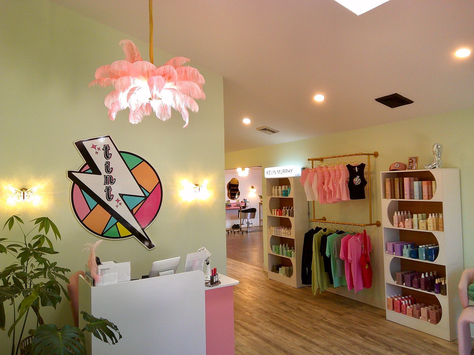 Bright boutique interior with clothing racks, colorful wall art, plants, and a pink pendant light