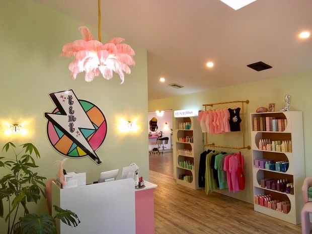 Colorful boutique interior with clothing racks, wall art, shelves, and a pink hanging light