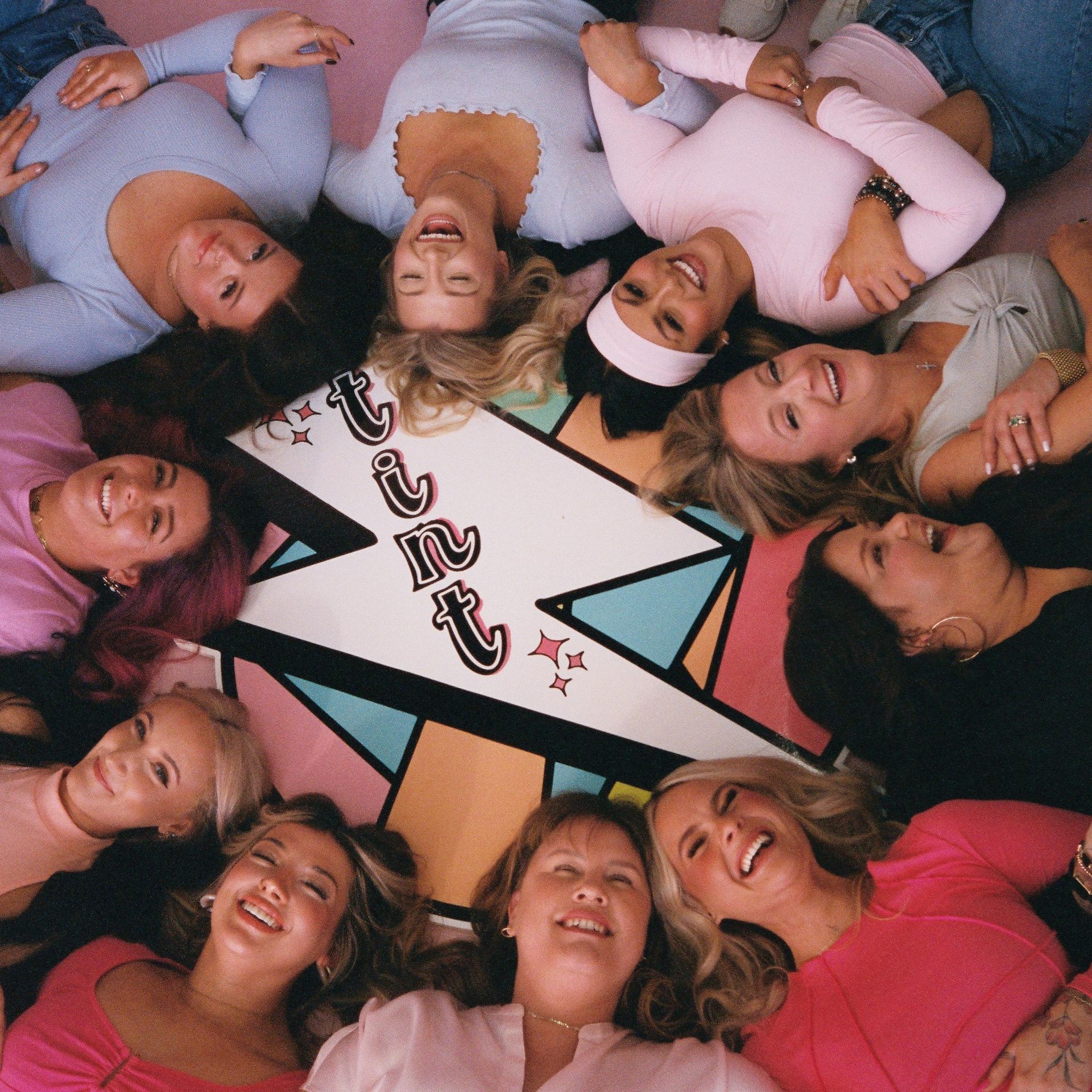 People lying in a circle around a colorful star sign, smiling at the camera.