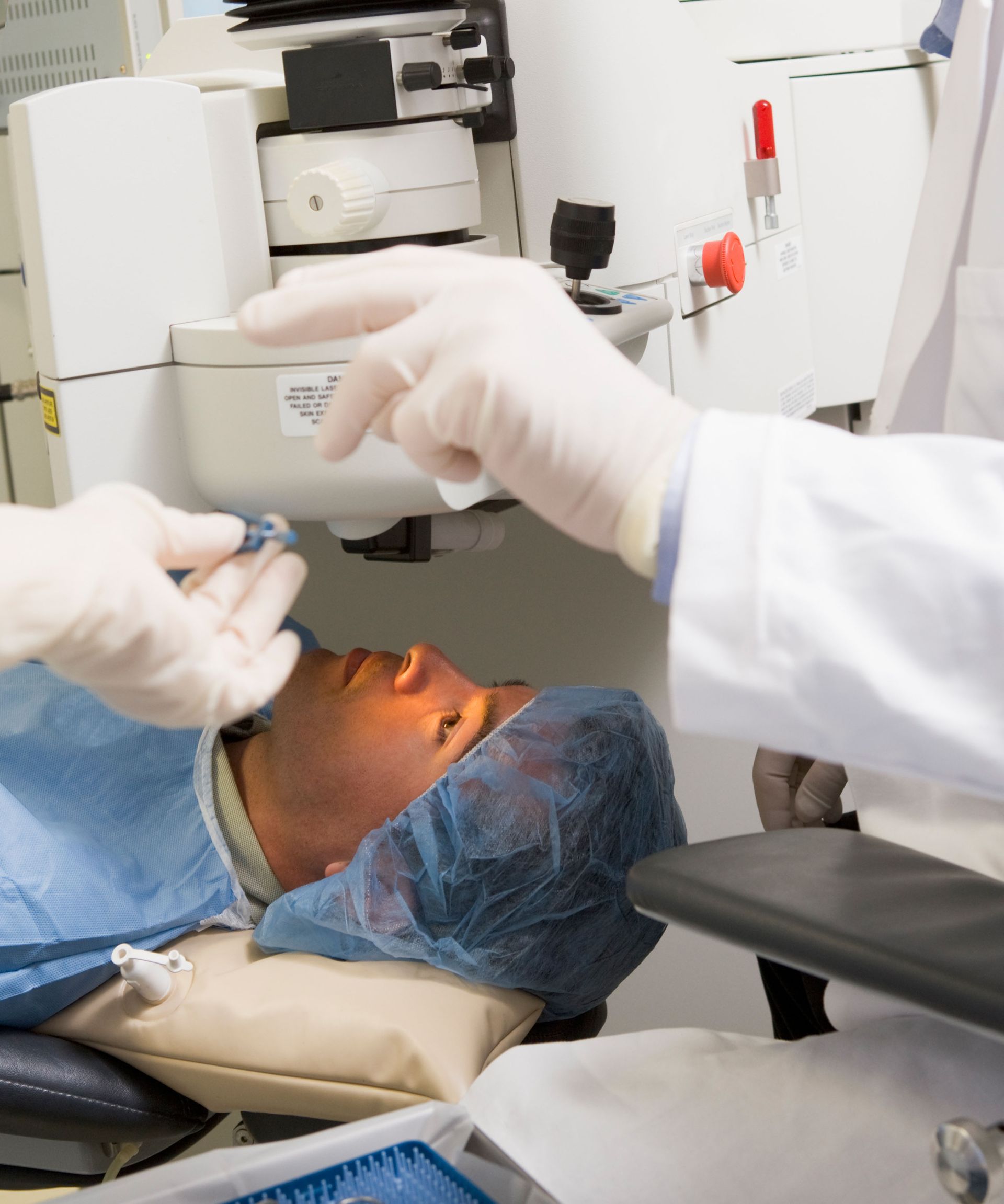 A person in a surgical gown is getting their eyes examined by a doctor