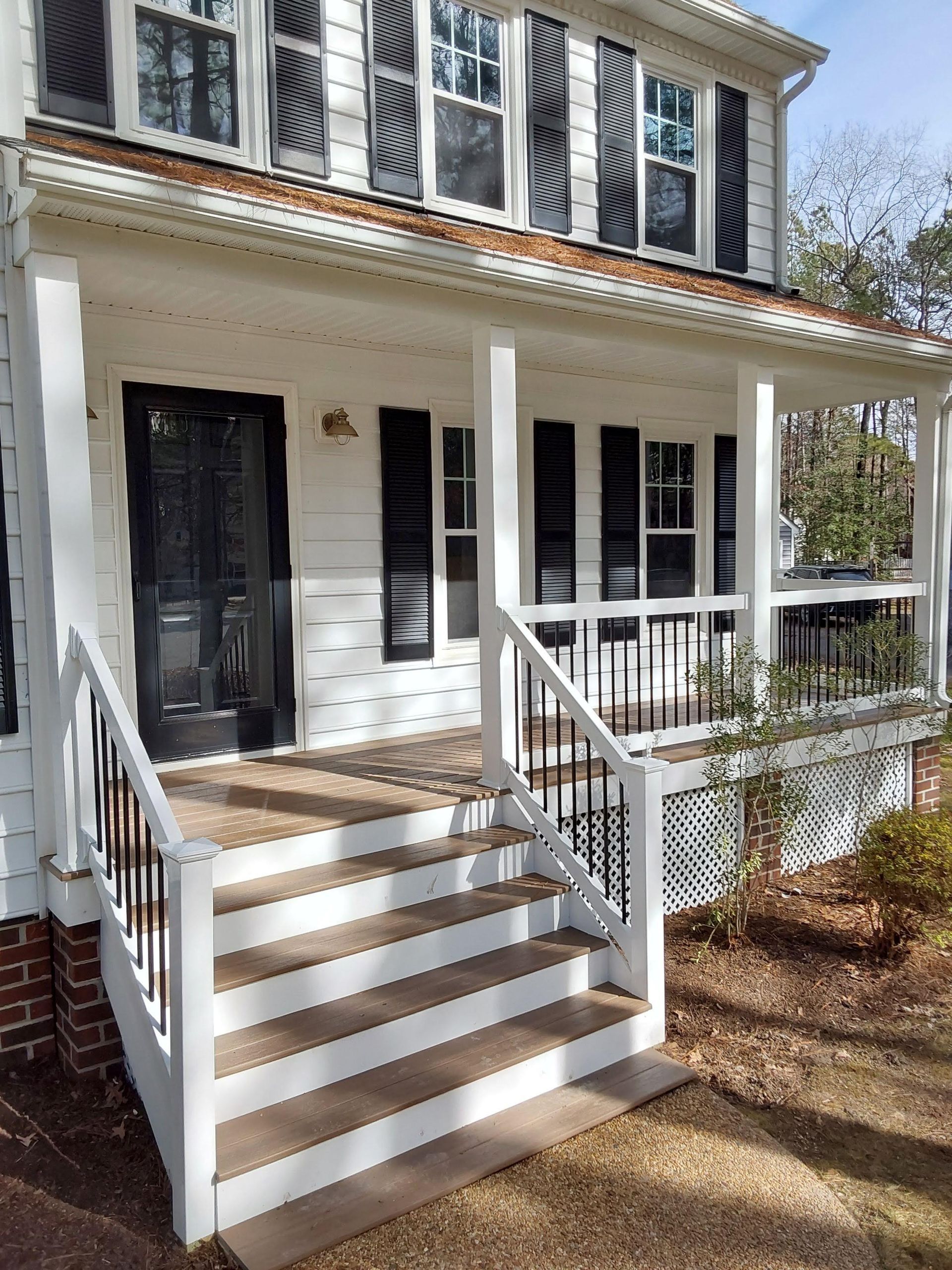 White house with porch, steps, black door and shutters.