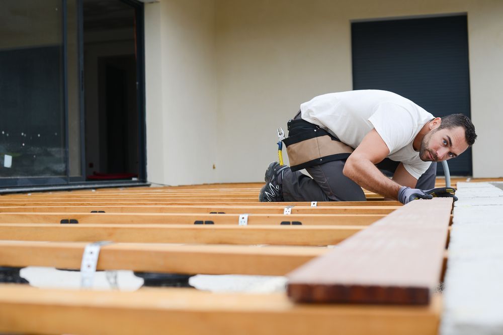 A person installing wooden deck boards with tools, outdoors.
