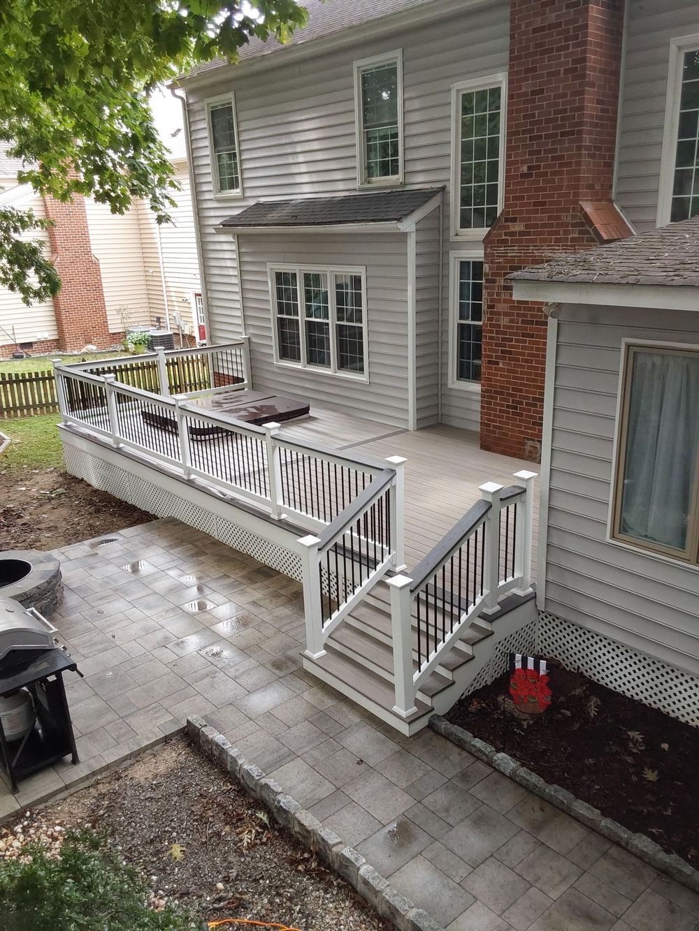 Backyard patio with stairs, railing, and a hot tub next to a two-story gray house.