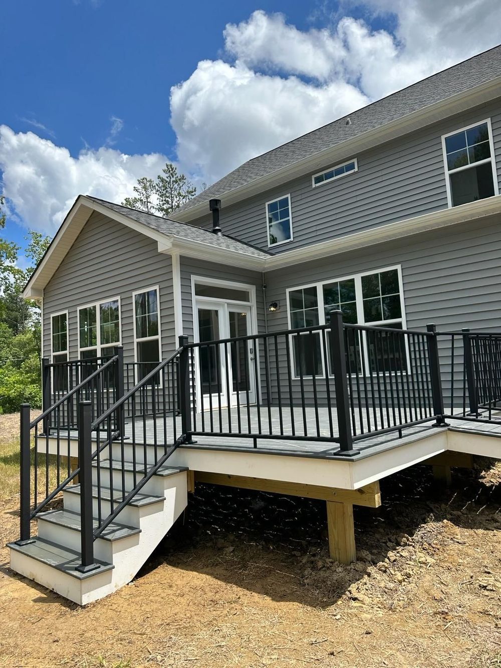 Two-story house with a gray exterior, deck with black railing and stairs, and a clear sky.