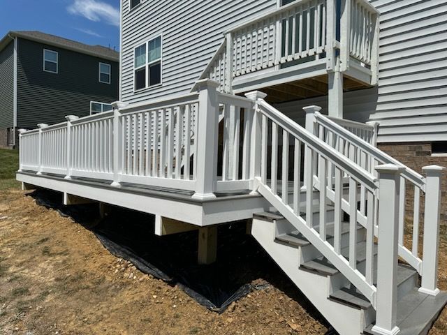 White deck with railing and stairs, attached to a gray-sided house on a sloped yard.