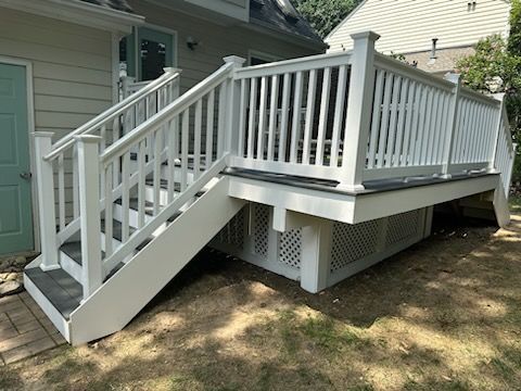 White deck with stairs, railing, and lattice skirting, attached to a house with a green door.