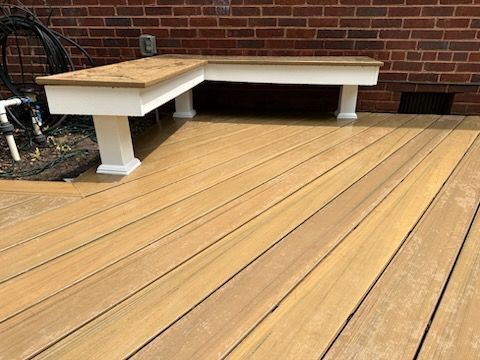 L-shaped bench on a wooden deck against a brick wall. The bench is white with a brown top.
