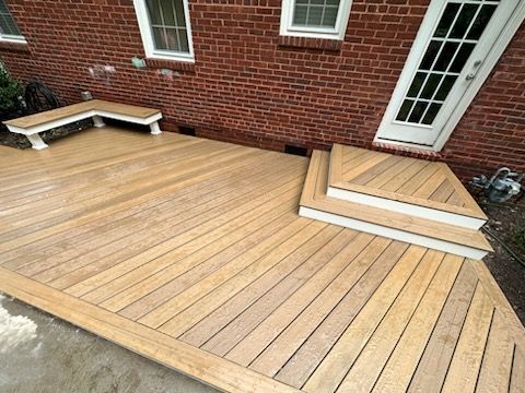 Wooden deck with built-in bench and steps next to a brick building with a white door.