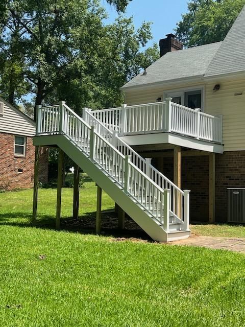 Raised white deck with stairs attached to a yellow house with a green lawn.