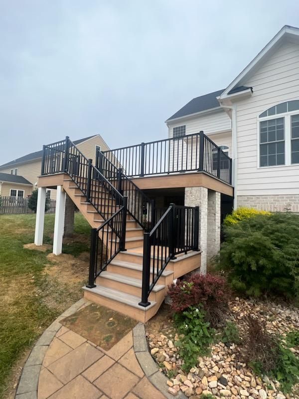 Deck with black railings and stairs leading to a house with white siding on a cloudy day.