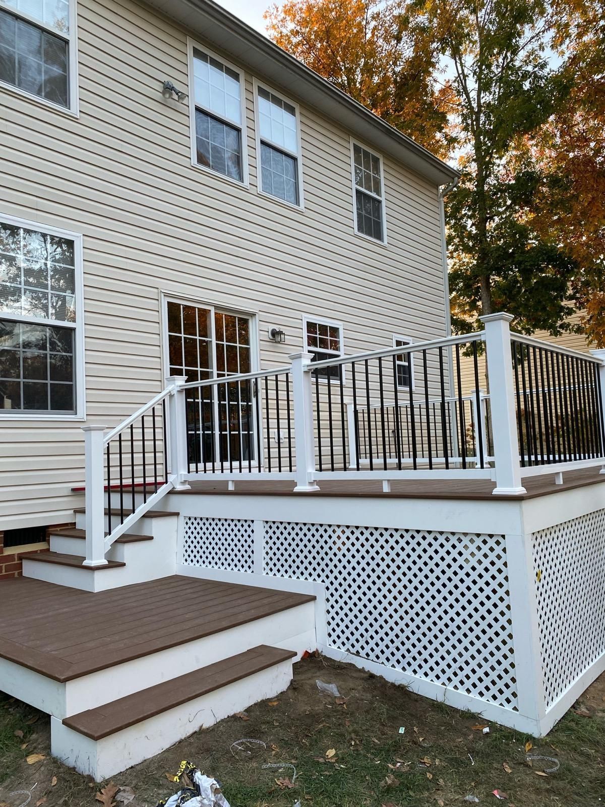 Back of a house with a multi-level deck featuring white railings, brown steps, and decorative lattice.