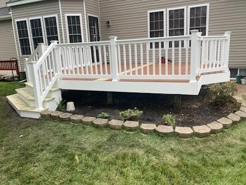 White deck with stairs, surrounded by a small garden and grass, next to a tan house.