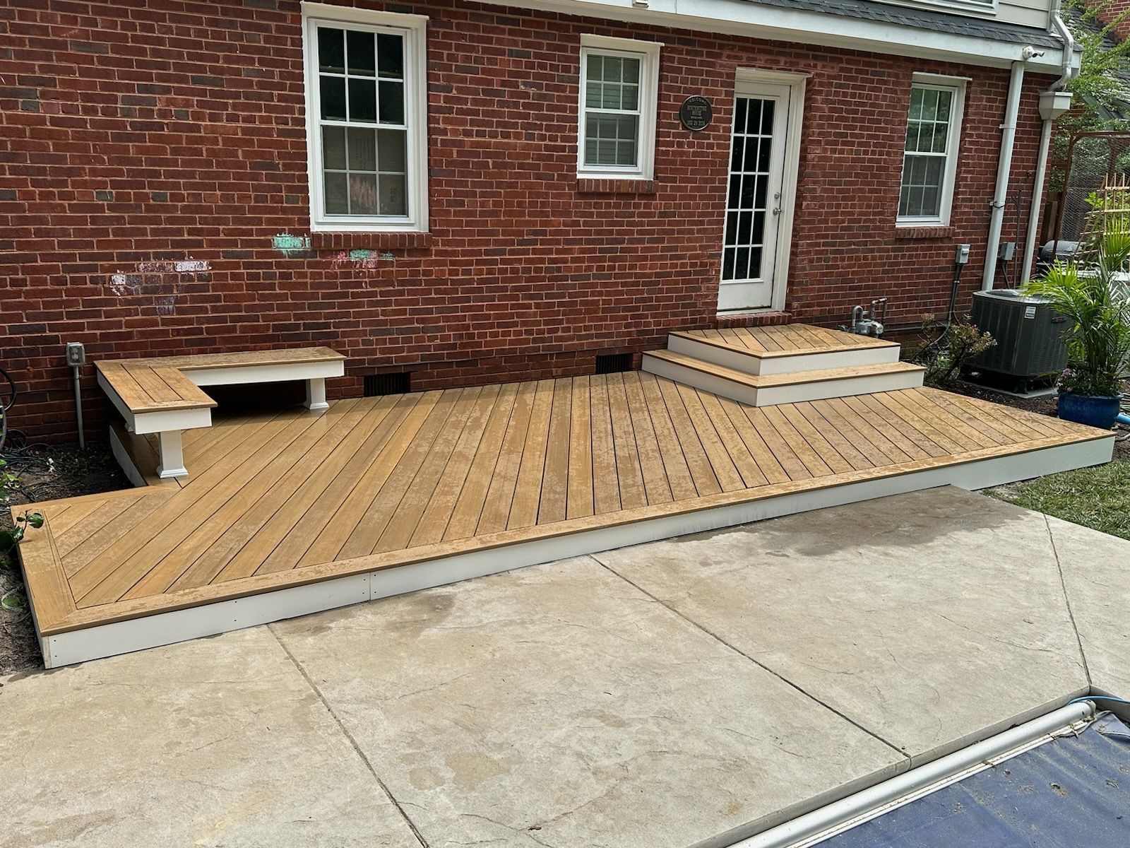 A wooden deck with a built-in bench and steps, against a red brick building.