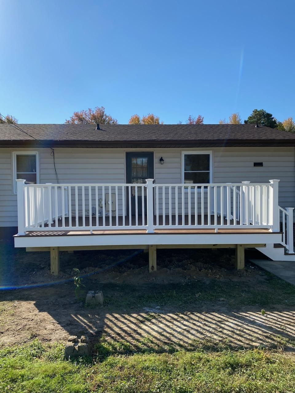 White-railed deck with brown boards, attached to a light-colored house. Clear blue sky.