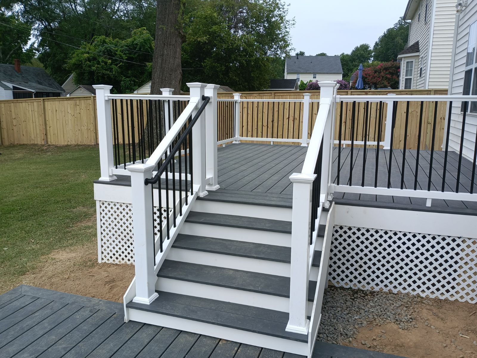 Composite deck with stairs and black railings, surrounded by a fence and a house.