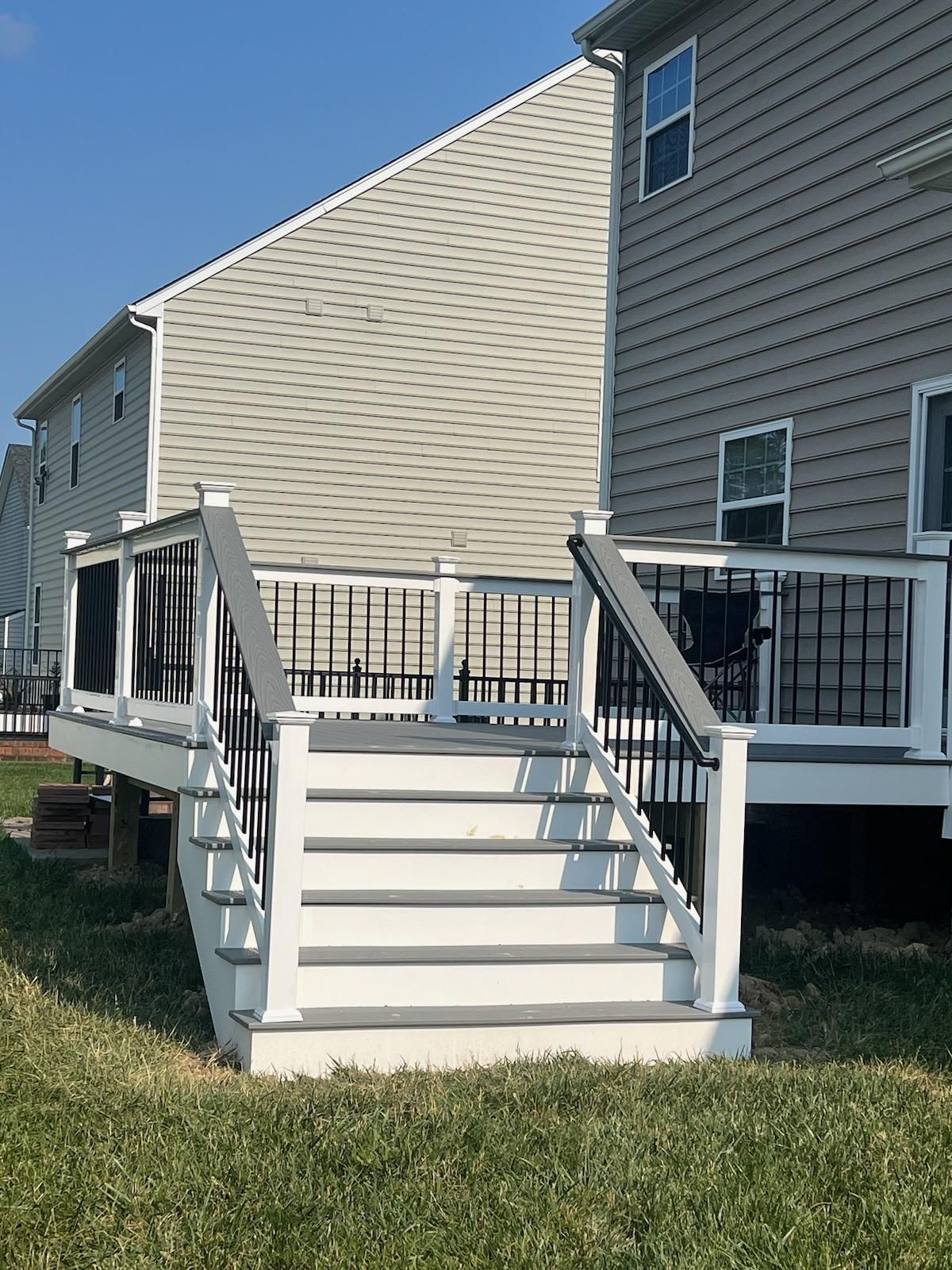 A gray and white deck with stairs, attached to a light gray house, set on green grass.