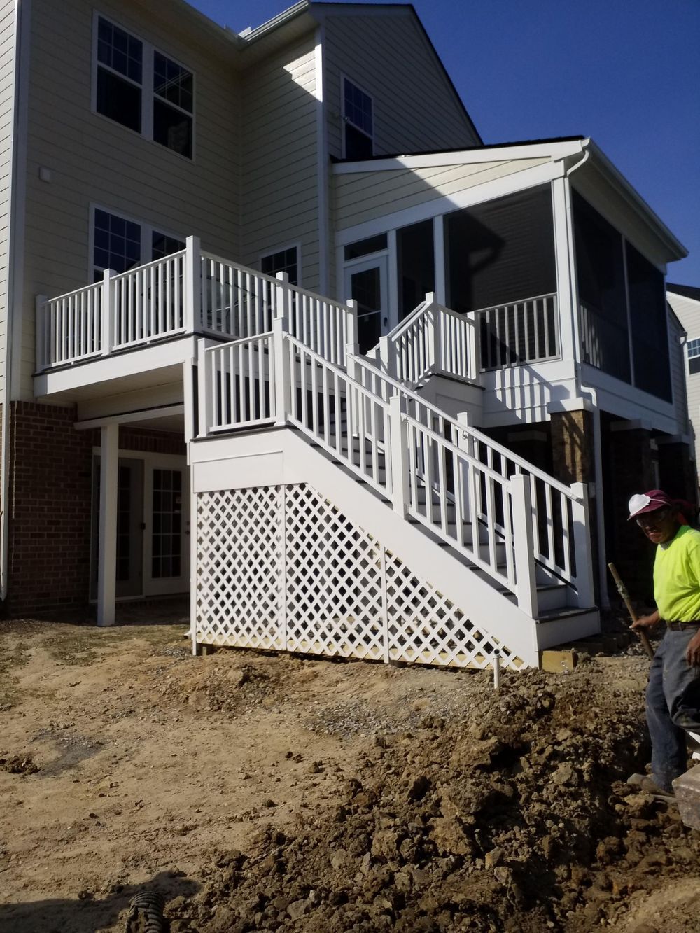 White deck with stairs leading to a screened porch on the back of a house; a person in a yellow shirt stands to the right.