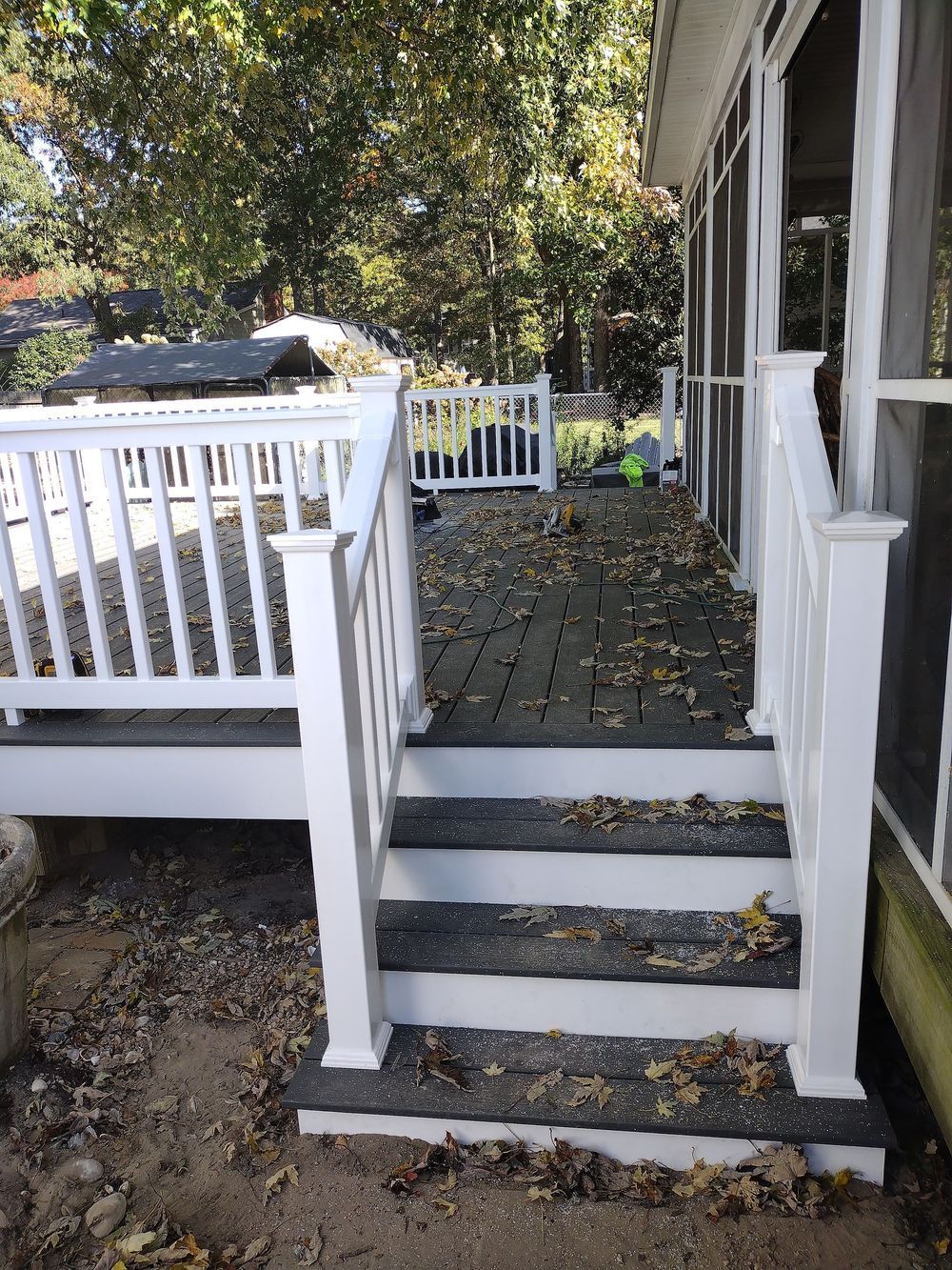 White railing and stairs lead to a deck covered in leaves.
