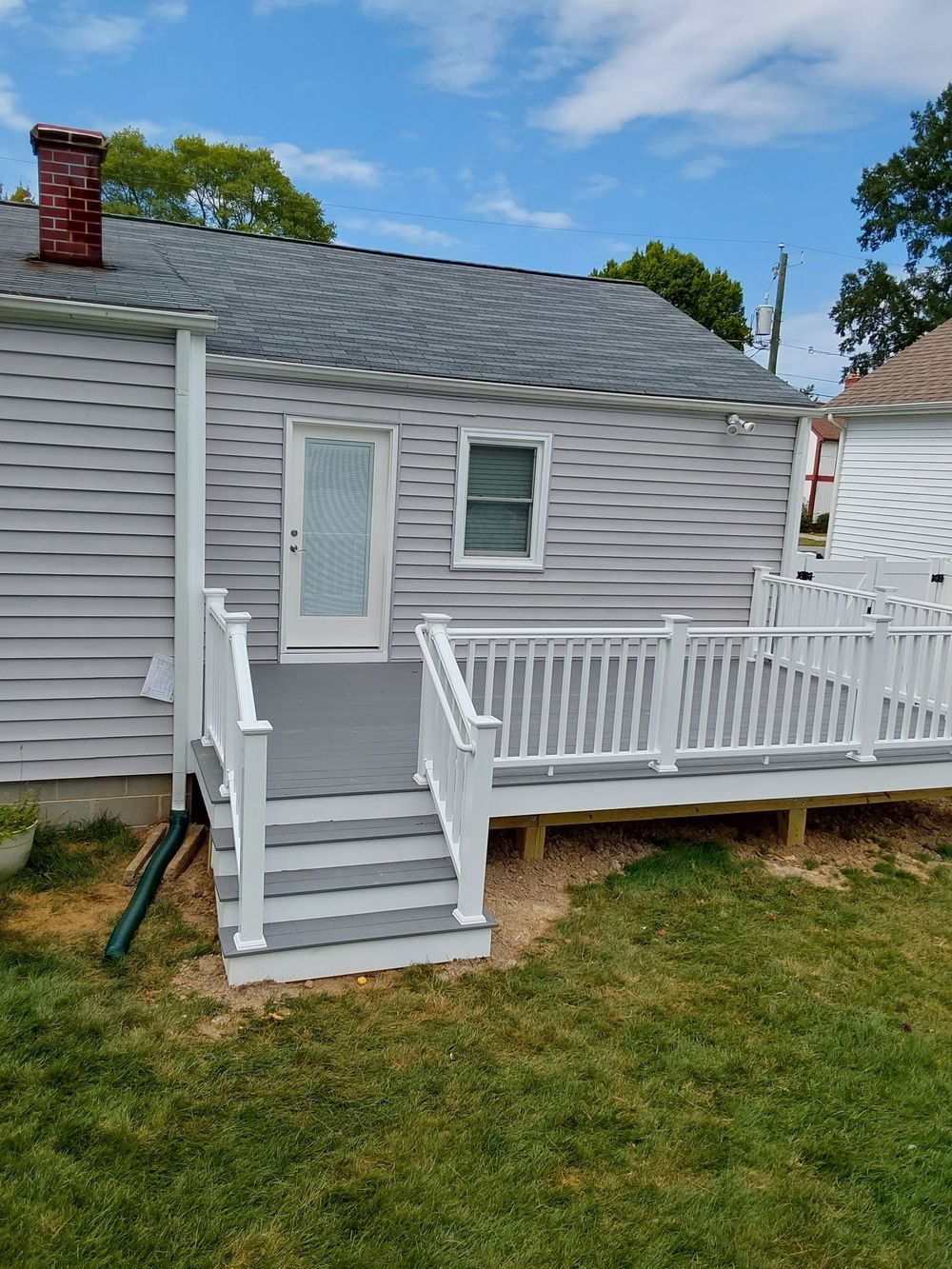 Back of a house with gray siding, a deck, steps, white railings, a door, and a window.