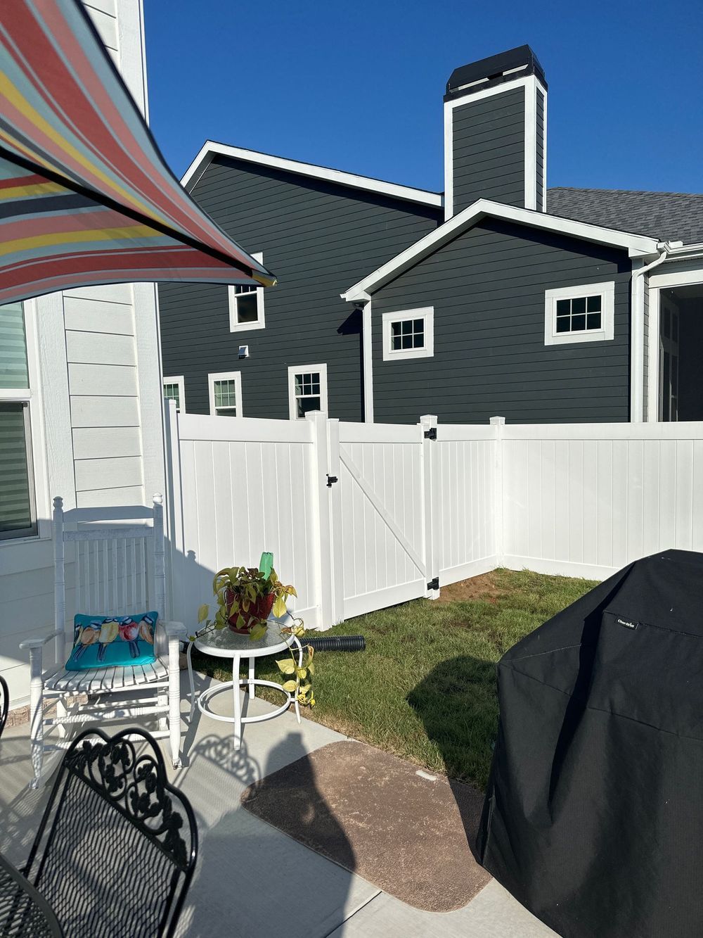 White fence with yard, patio furniture, and dark-gray building under a blue sky.