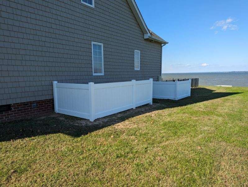 White fence enclosures alongside a house with windows, grass lawn, and water in the background.