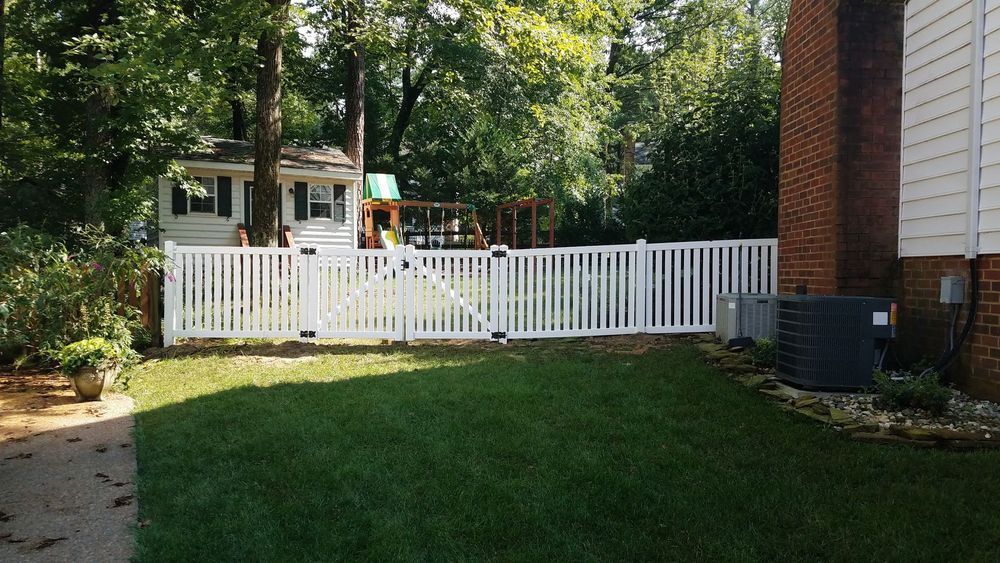 White picket fence surrounding a backyard with a playhouse and mature trees.