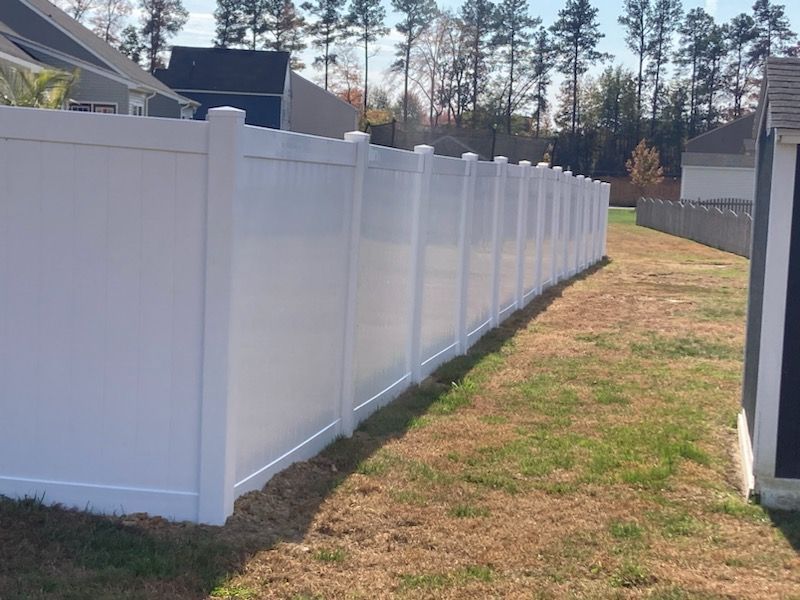 White vinyl fence in a backyard, separating properties with trees in the background.