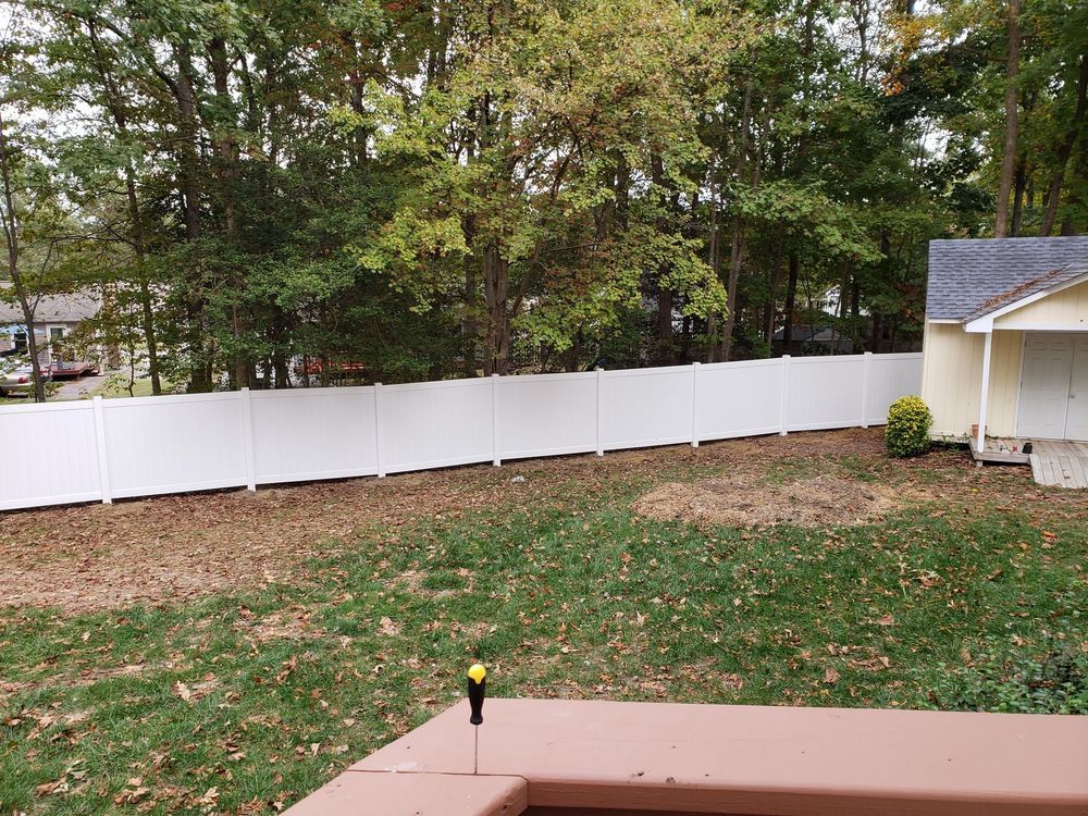White fence bordering a backyard with trees in the background. A small, yellow building is to the right.
