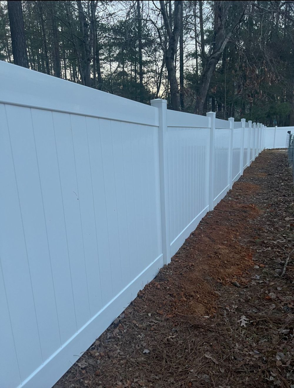 White vinyl fence in a yard, extending towards trees in the background.