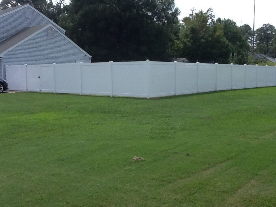 White vinyl privacy fence surrounding a grassy yard next to a house.