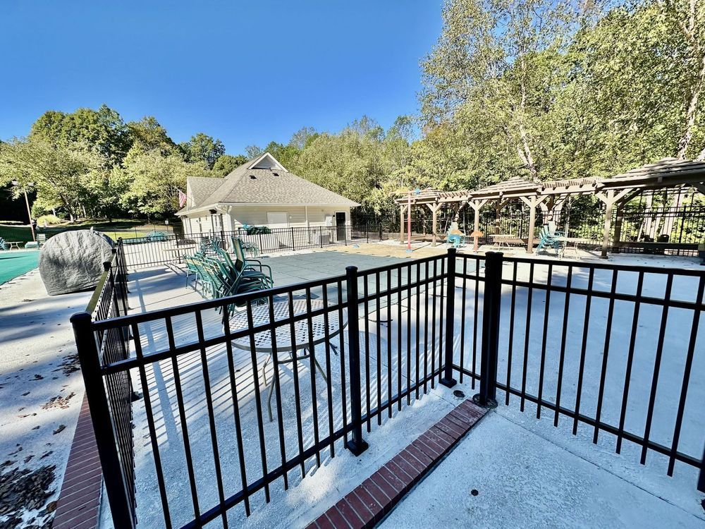 Pool area with black fence, pavilion, and pergola surrounded by trees.