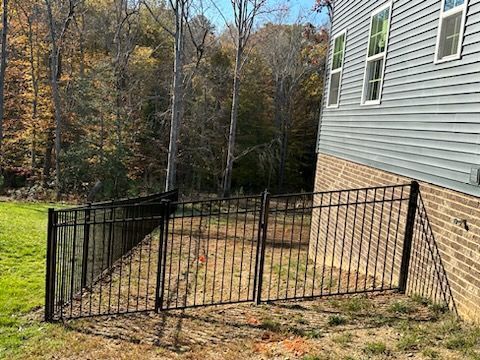 Black metal fence surrounding a yard area next to a house, autumn foliage in the background.