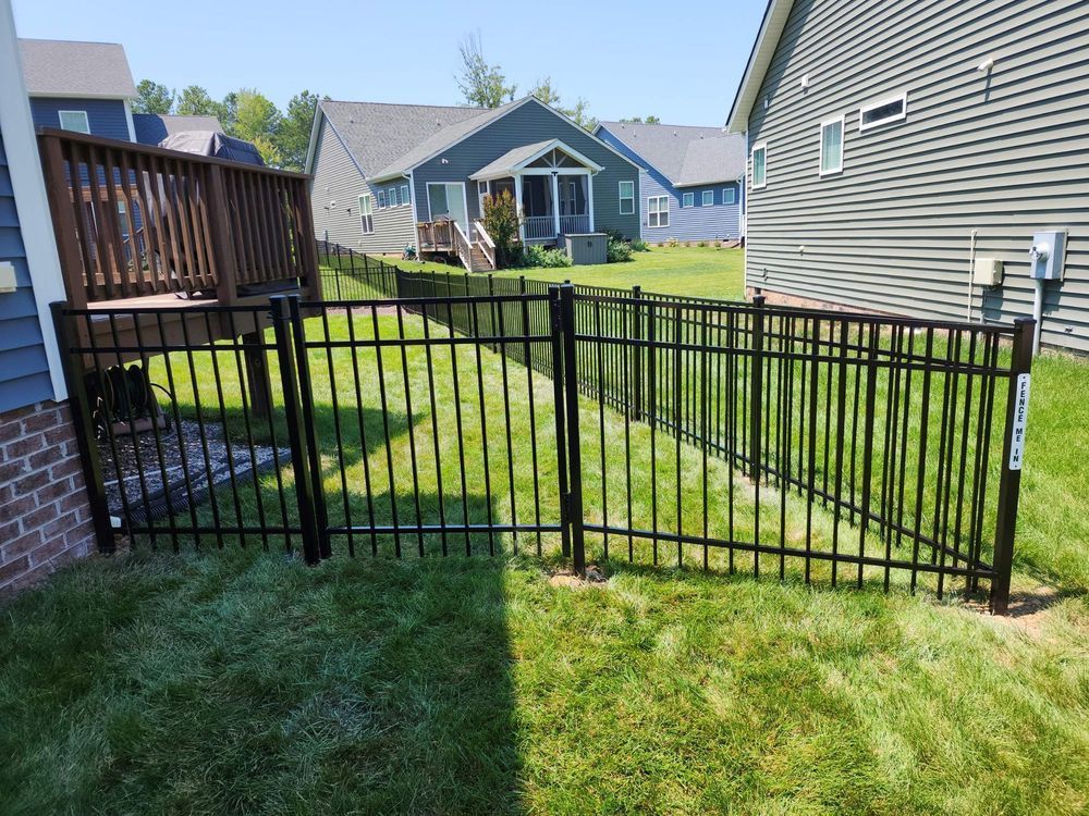 Black metal fence surrounds a grassy yard between two houses, sunny day.