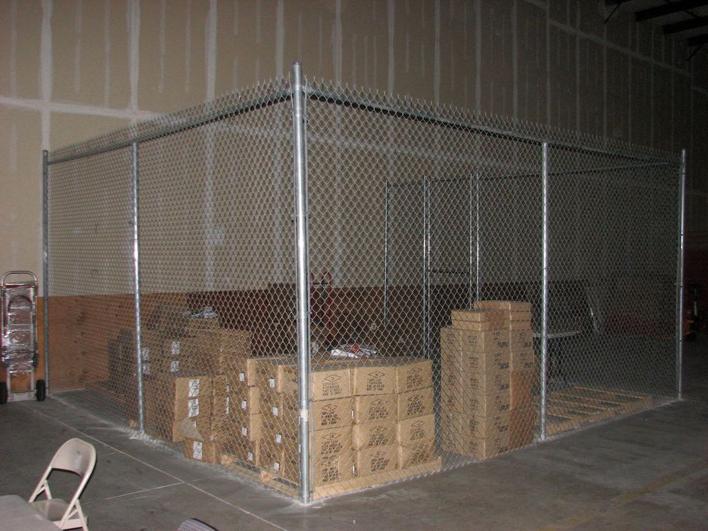 A chain-link security cage inside a warehouse filled with cardboard boxes on pallets.