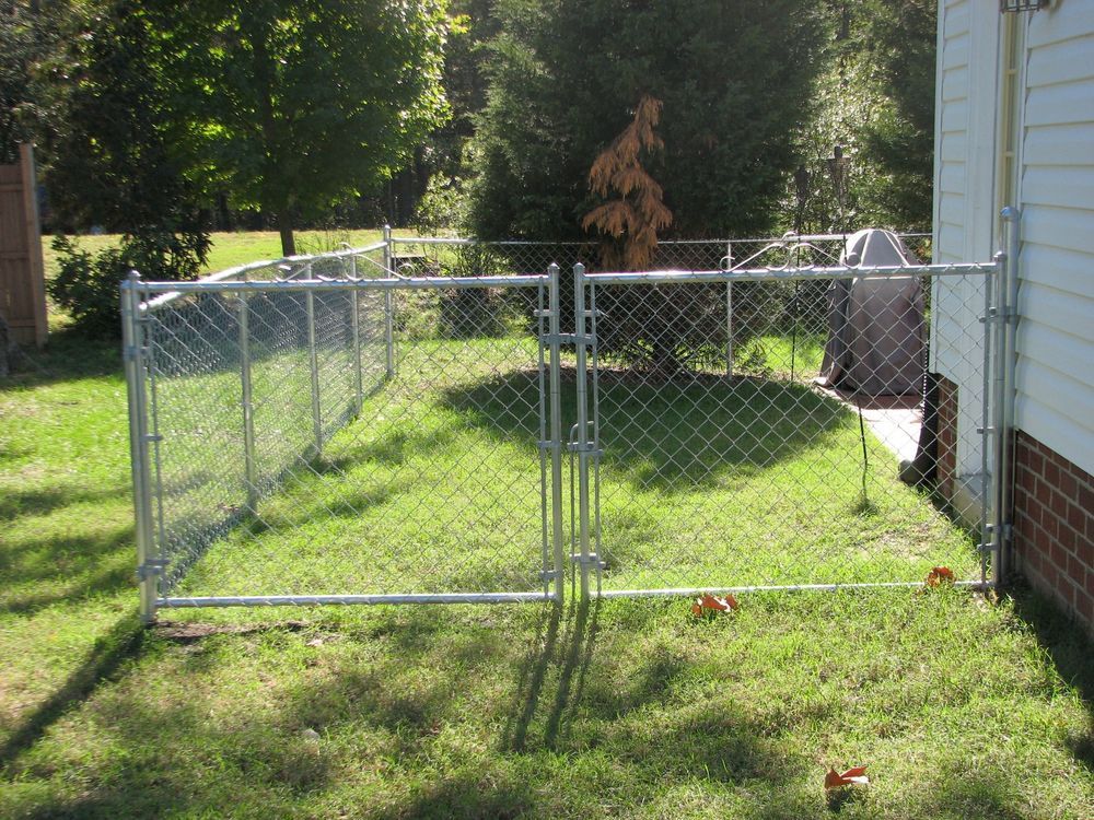 Chain link fence enclosing a small grassy yard, with a gate and a house on the right.